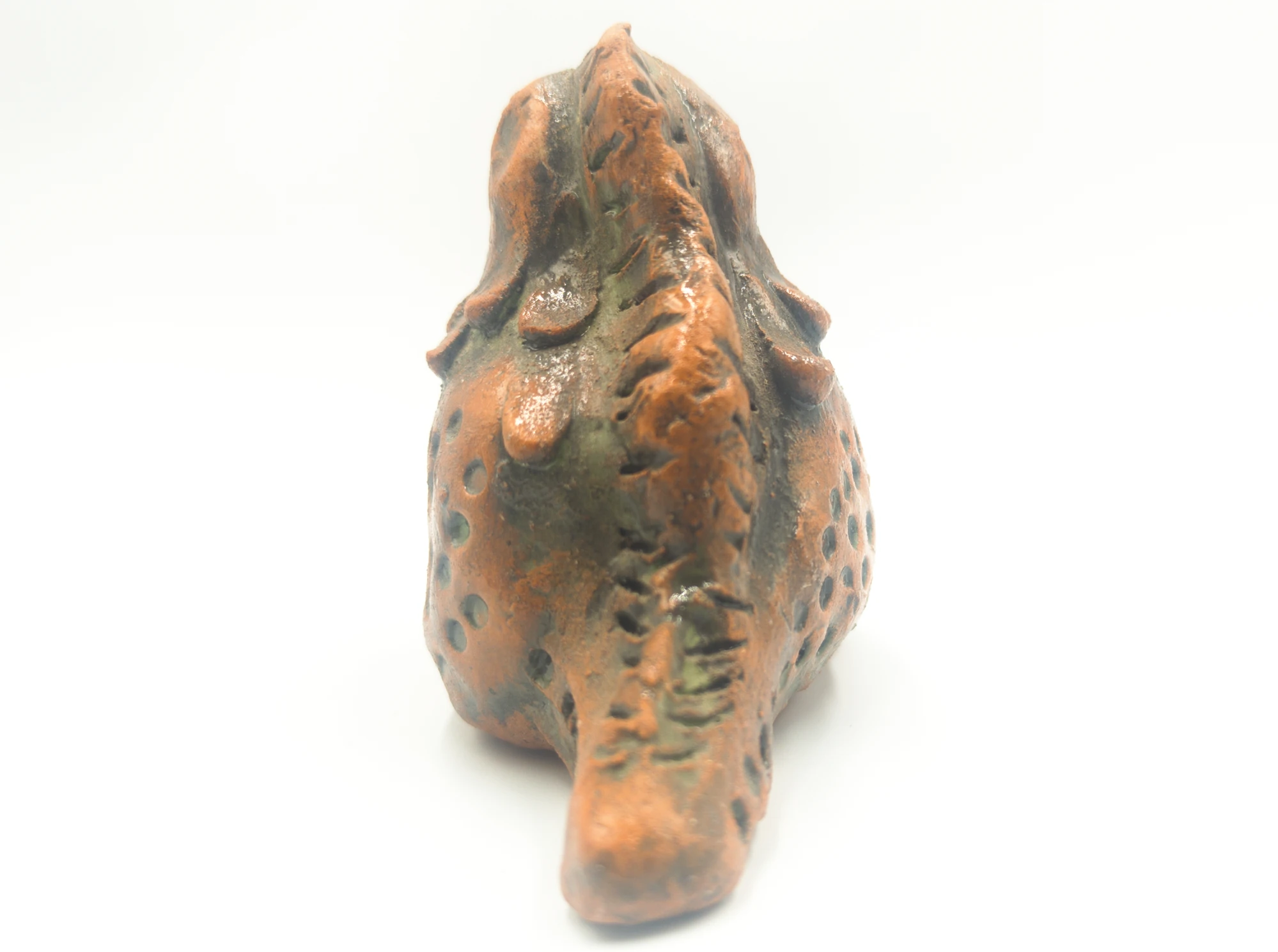 Glazed ceramic dinosaur seen from behind, showing its tail and ridge along the back.